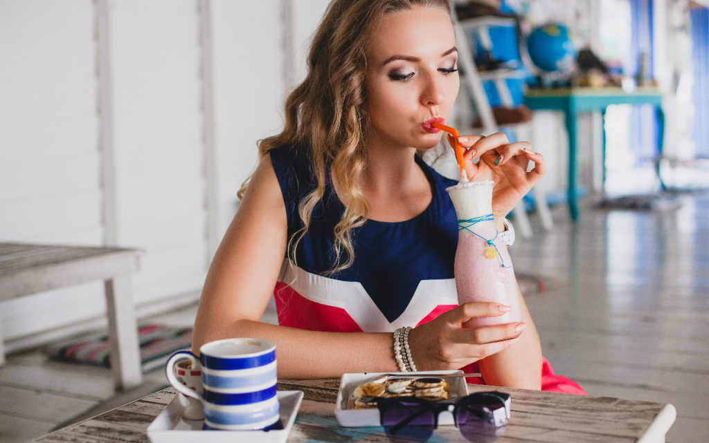 molodaa-stil-naa-krasivaa-zensina-v-morskom-kafe-p-et-kokteil-nyi-smuzi-solncezasitnye-ocki-koketlivyi-kurortnyi-stil-modnyi-narad-ulybaetsa-plat-e-morskih-cvetov (1).jpg