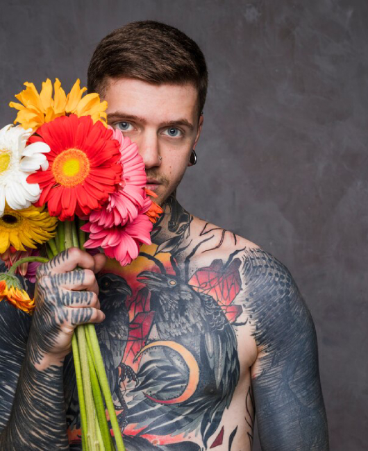 hipster-tattooed-young-man-holding-colorful-gerbera-flowers-hand-standing-against-grey-backdrop_23-2148121976.jpg