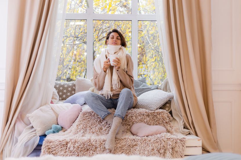 warm-portrait-woman-sitting-windowsill-with-cup-hot-tea-coffee-wearing-sweater-white-scarf.jpg