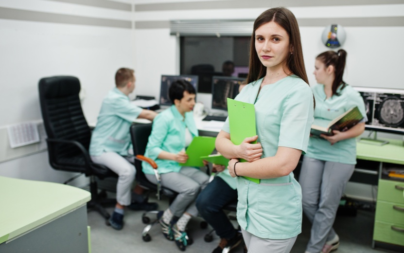 medical-theme-portrait-female-doctor-with-clipboard-against-group-doctors-meeting-mri-office-diagnostic-center-hospital (1).jpg