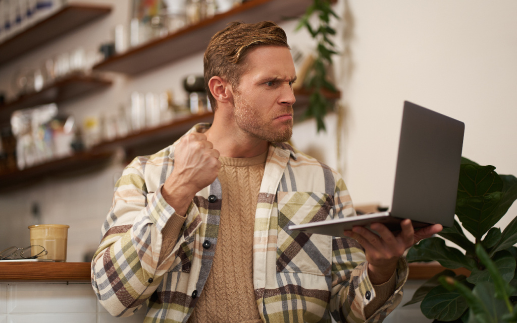 portret-serditogo-celoveka-v-kafe-s-noutbukom-gladasim-na-ekran-i-pokazyvausim-szatyi-kulak-vo-vrema (1).jpg