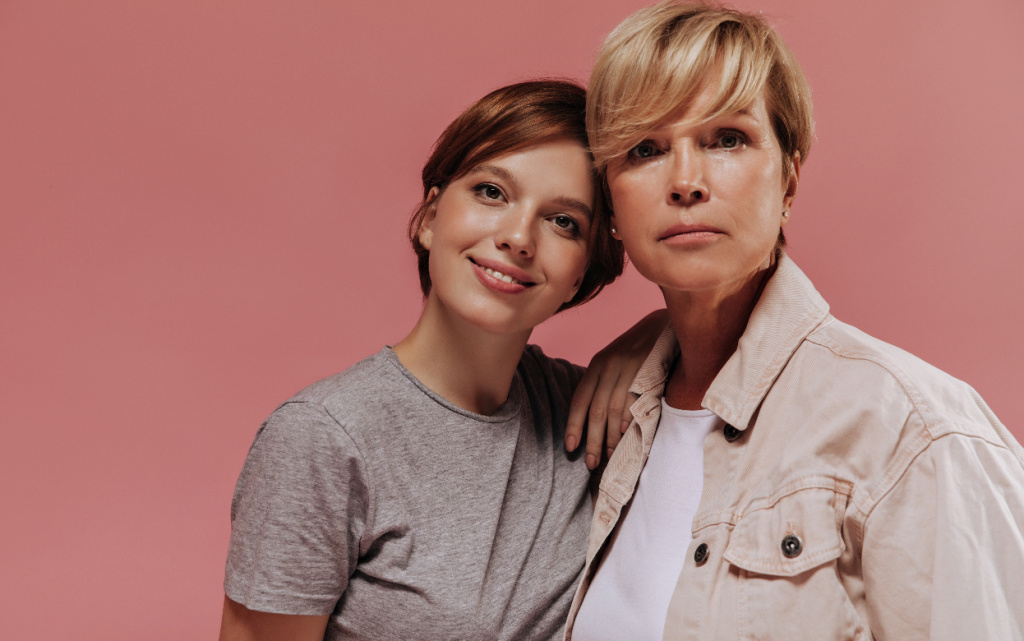 ser-eznaa-staruha-so-svetlymi-volosami-v-krutoi-kurtke-smotrit-v-kameru-vmeste-s-ulybauseisa-devuskoi-s-volosami-brunetki-v-seroi-futbolke-na-rozovom-fone (1).jpg