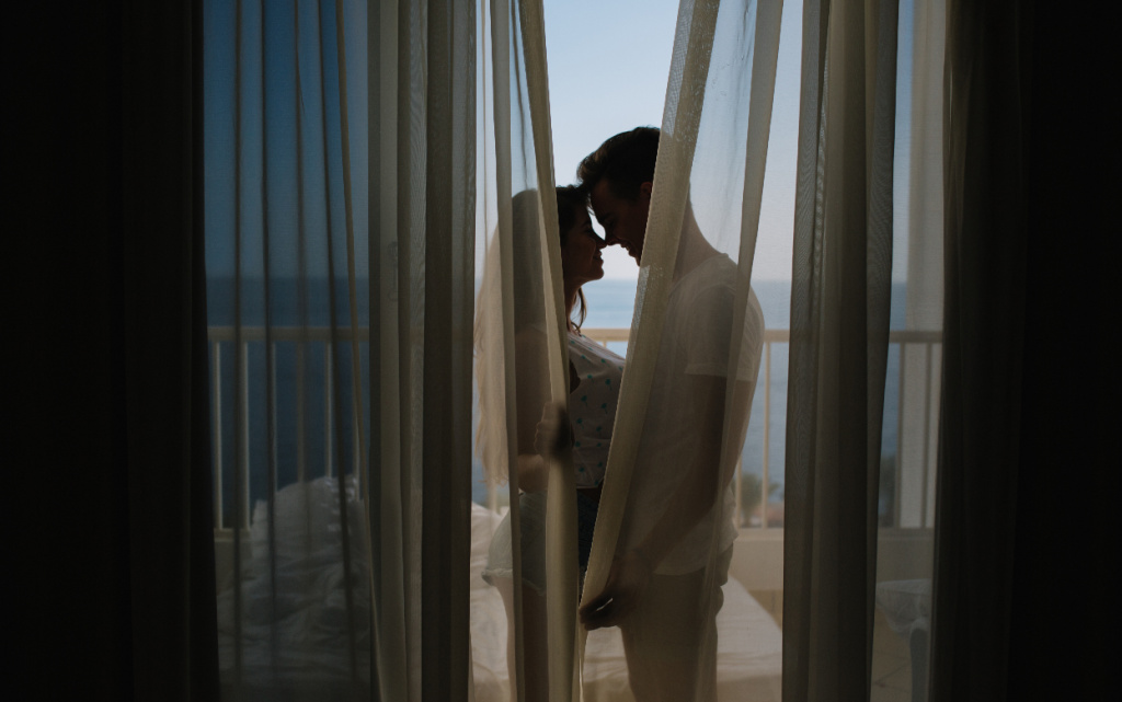 molodoi-celovek-priznaetsa-v-lubvi-svoei-ocarovatel-noi-podruge-stoa-na-balkone-za-storami-utrom-portret-krasivoi-pary-celuuseisa-na-terrase-posle-dolgogo-naprazennogo-dna (1).jpg