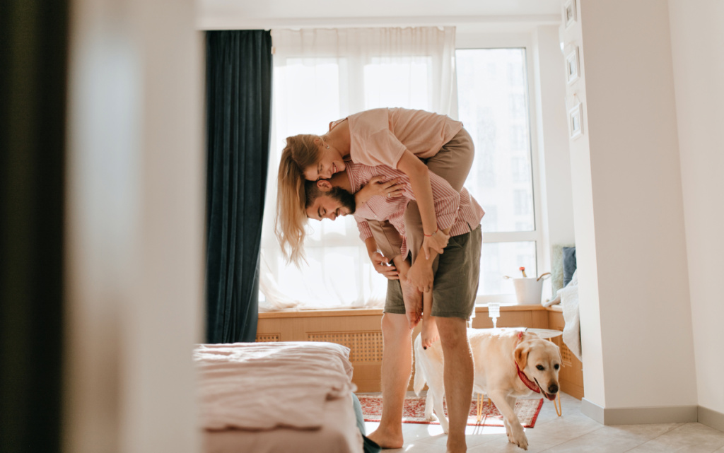 muzcina-v-sortah-cveta-haki-derzit-svou-moloduu-zenu-na-spine-a-ih-sobaka-idet-radom-vlublennye-naslazdautsa-bezzabotnymi-vyhodnymi-v-svoei-kvartire (1).jpg