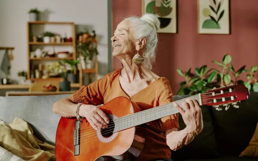 senior-woman-smiling-while-playing-acoustic-guitar-cozy-living-room-with-plants-paintings_249974-27738.jpg